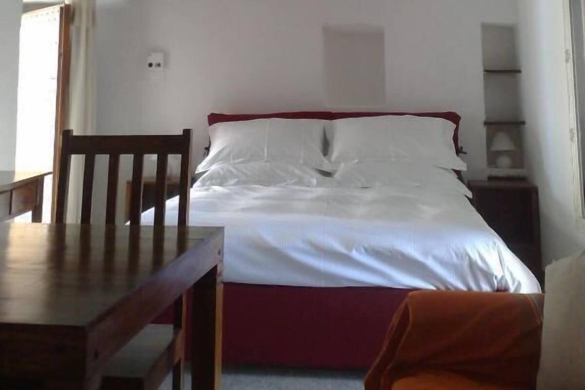 A bedroom with a bed, a wooden chair, a table, and a ceiling fan.