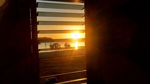 A sunset view through a window with horizontal blinds, a boat on the water, and a dog on the ground. - La Acuario Beach Inn (San Vicente)