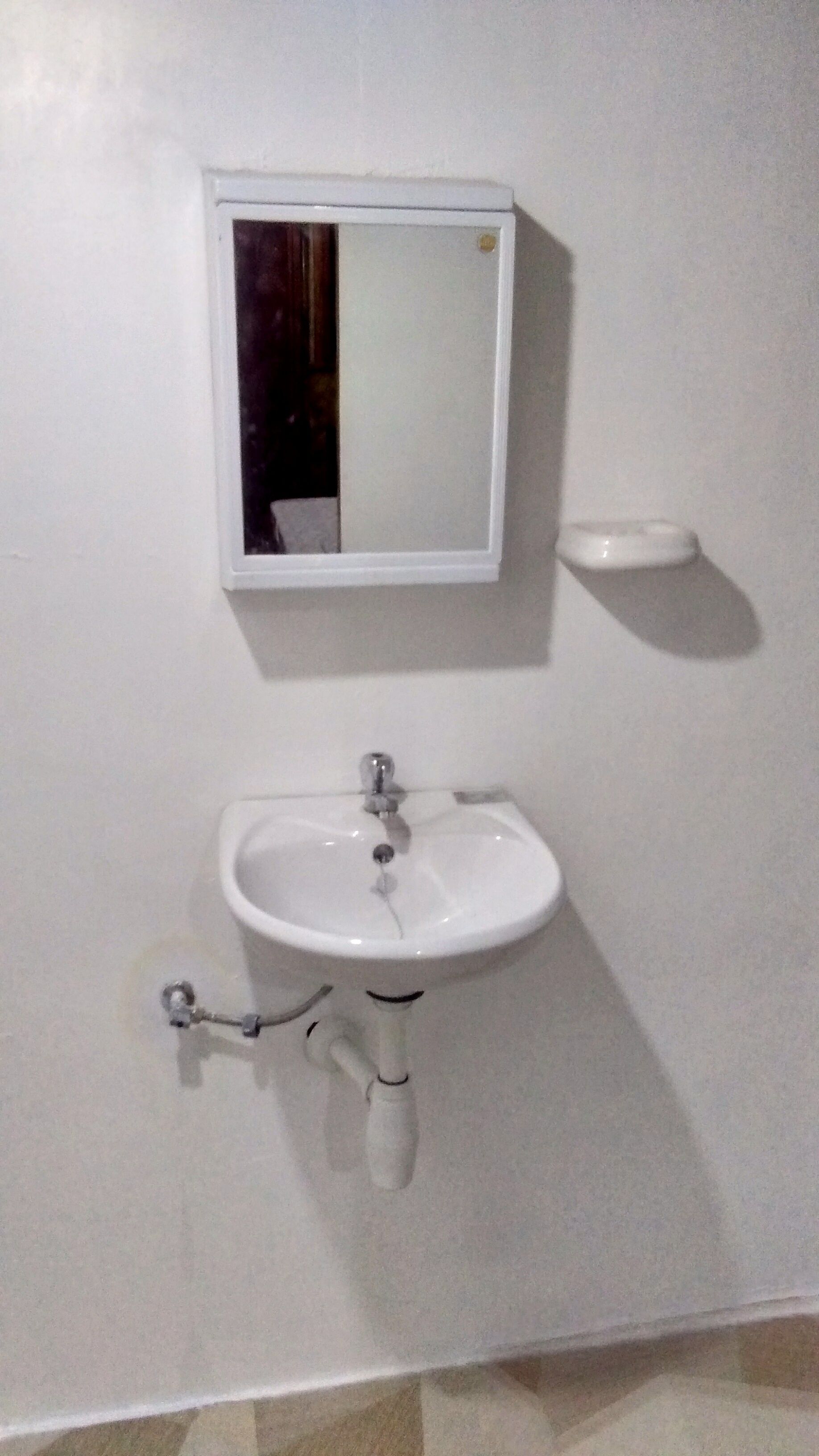 Un baño blanco con un espejo rectangular sobre un lavabo blanco.