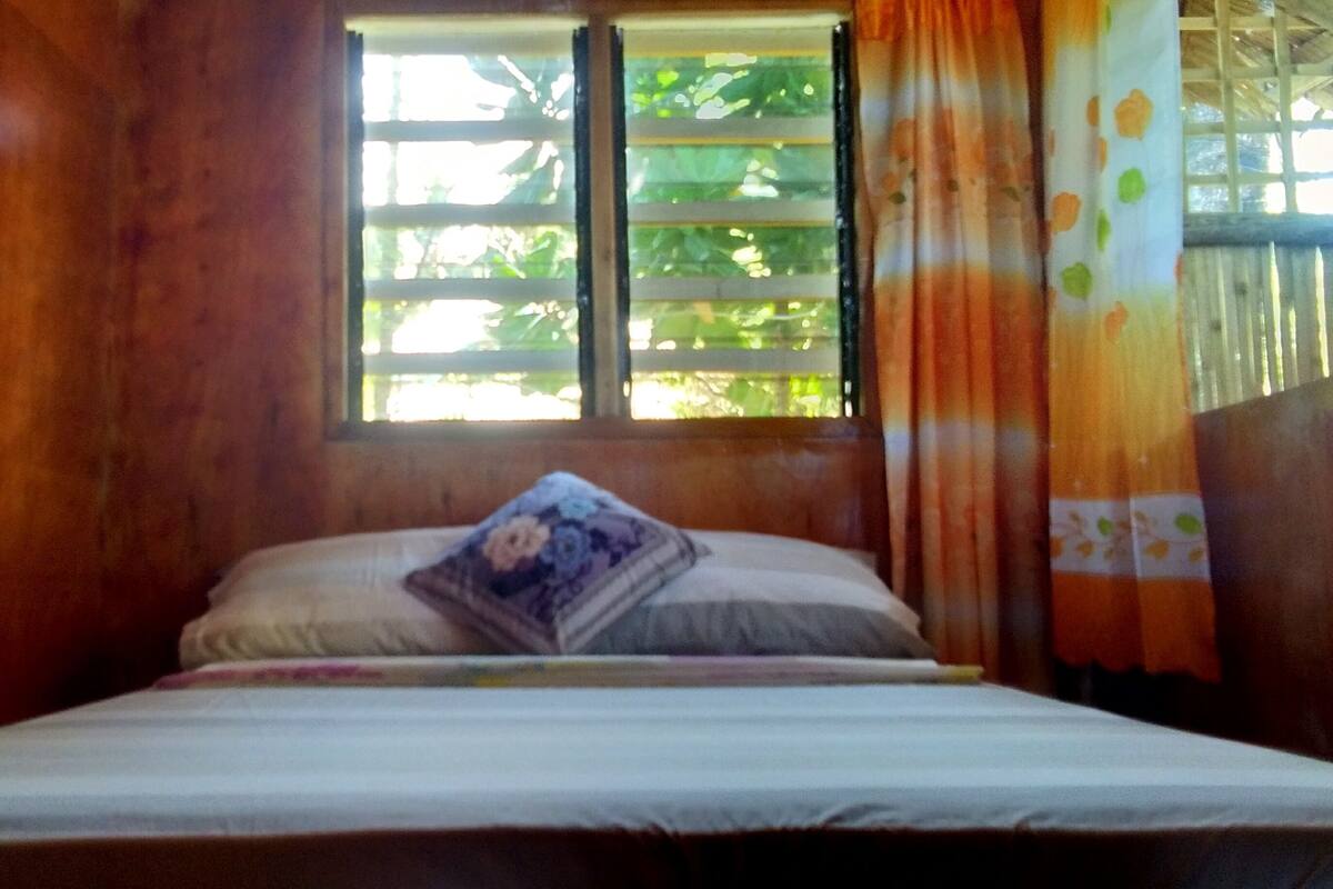 A bed with a floral pillow, a window with blinds, and curtains.