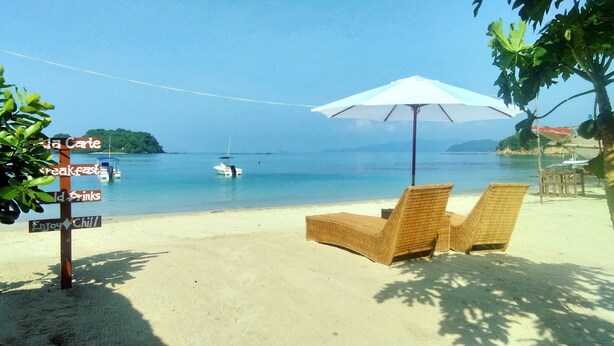 A beach with lounge chairs, a signpost with amenities, and a boat in the water. - La Acuario Beach Inn (San Vicente)
