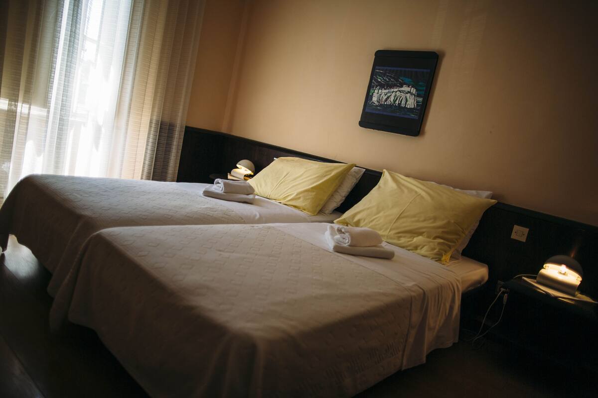 A hotel room with two beds, a nightstand, and a wall-mounted TV.