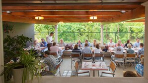 An outdoor dining area with multiple tables and chairs, surrounded by greenery and a covered roof structure. - Villa Amfora (Dubrovnik)