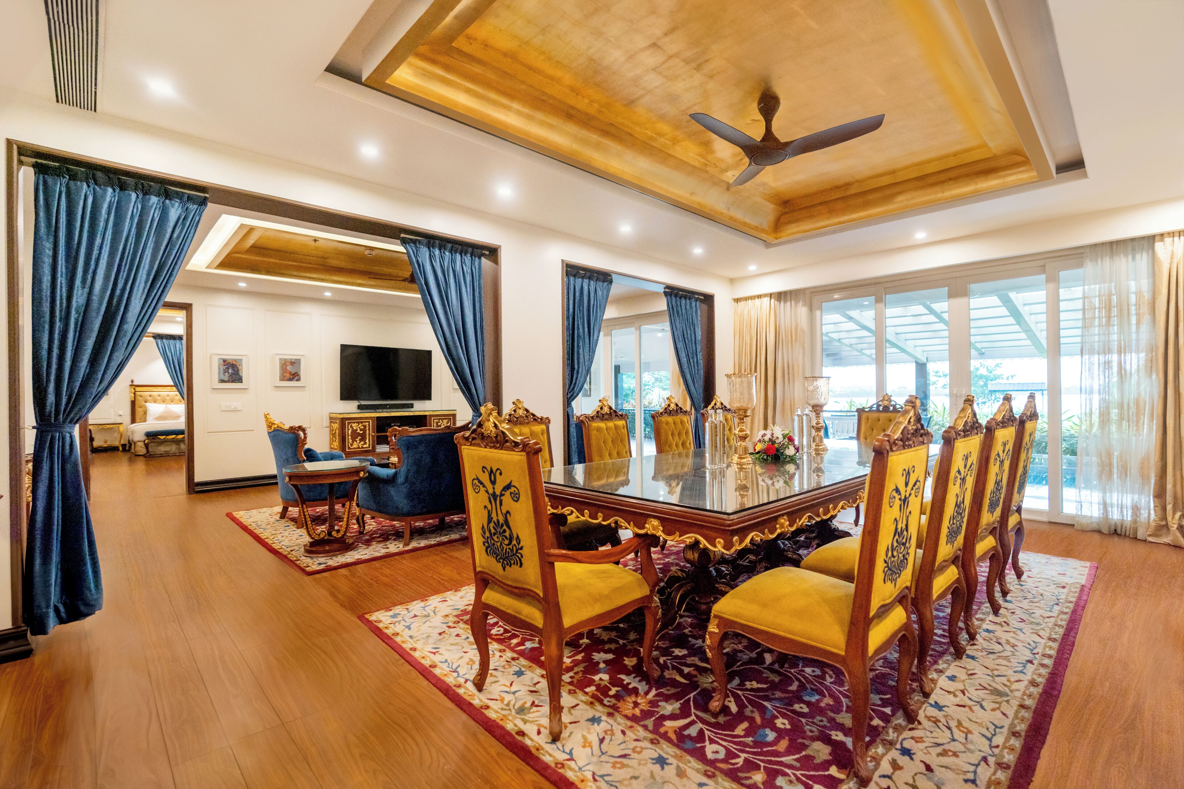 A spacious dining area with a large table and chairs, a ceiling fan, and large windows with curtains.