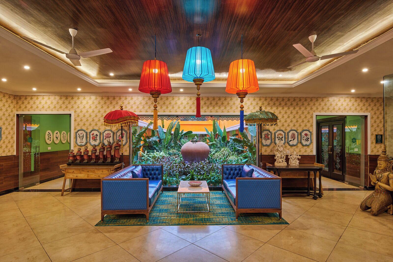 A lobby with a central seating area, decorative ceiling fans, and a lush indoor garden.
