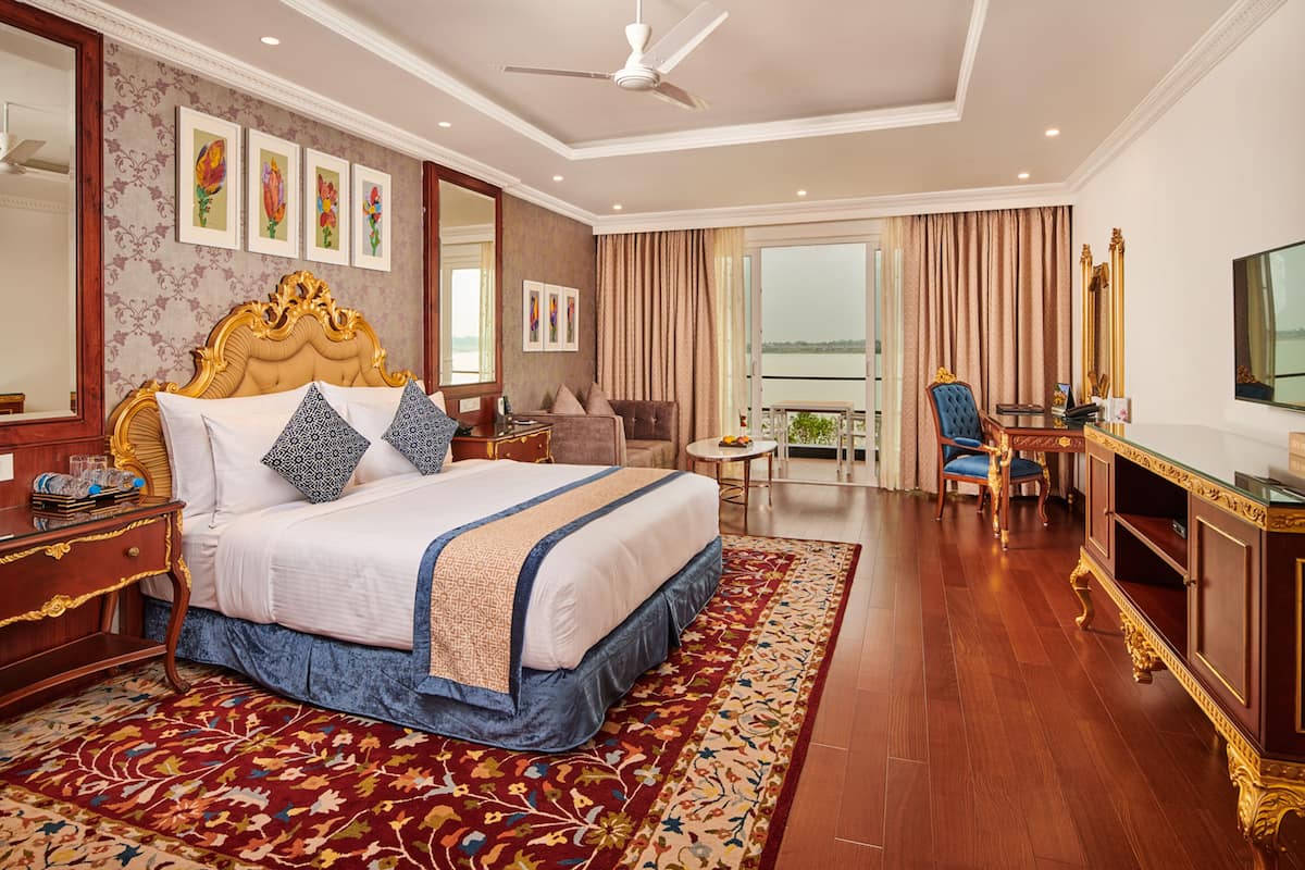 A spacious hotel room with a large bed, a desk, a chair, and a balcony with a view.