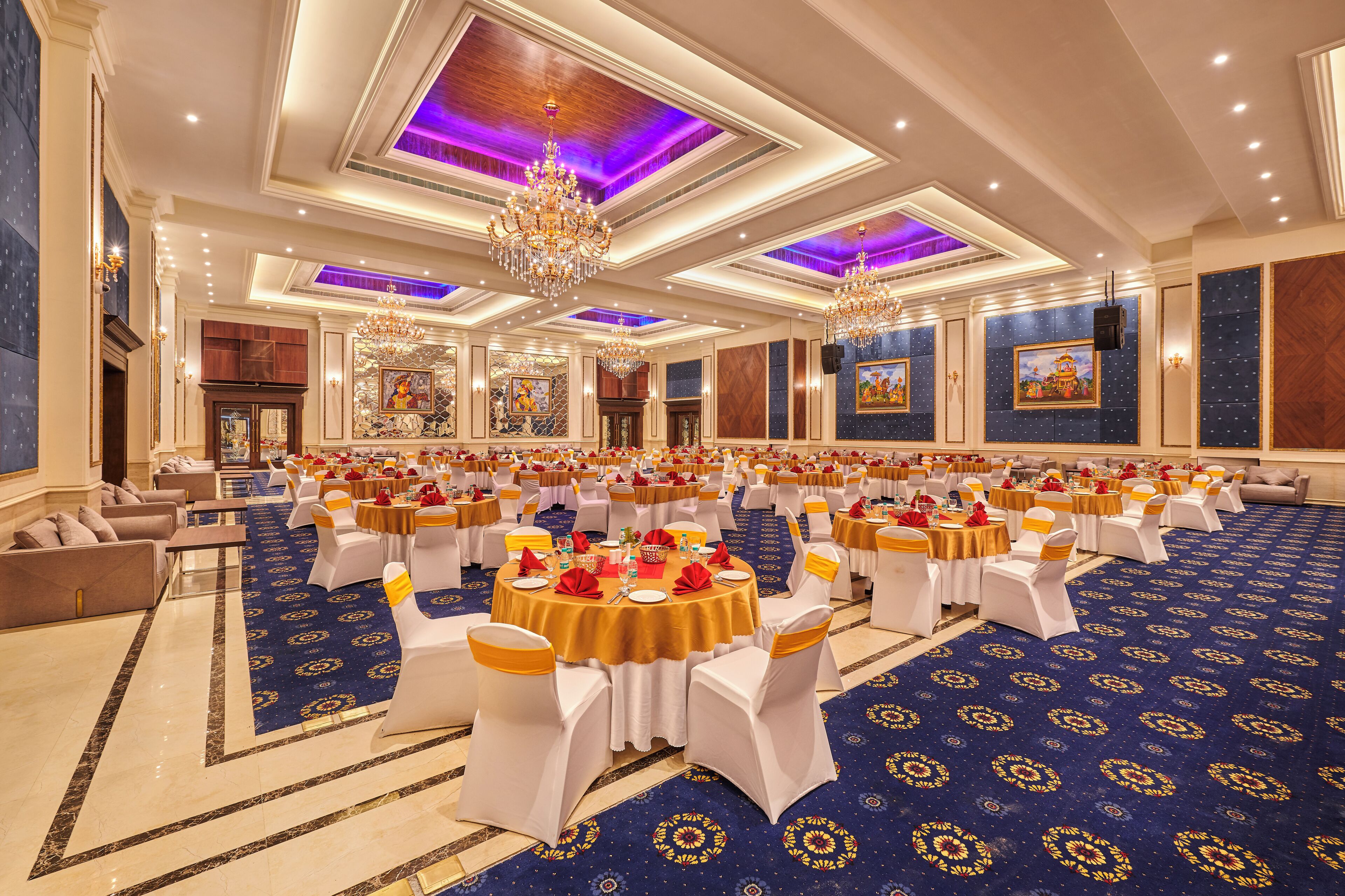 Een feestzaal met ronde tafels, witte stoelen en een blauw vloerkleed.