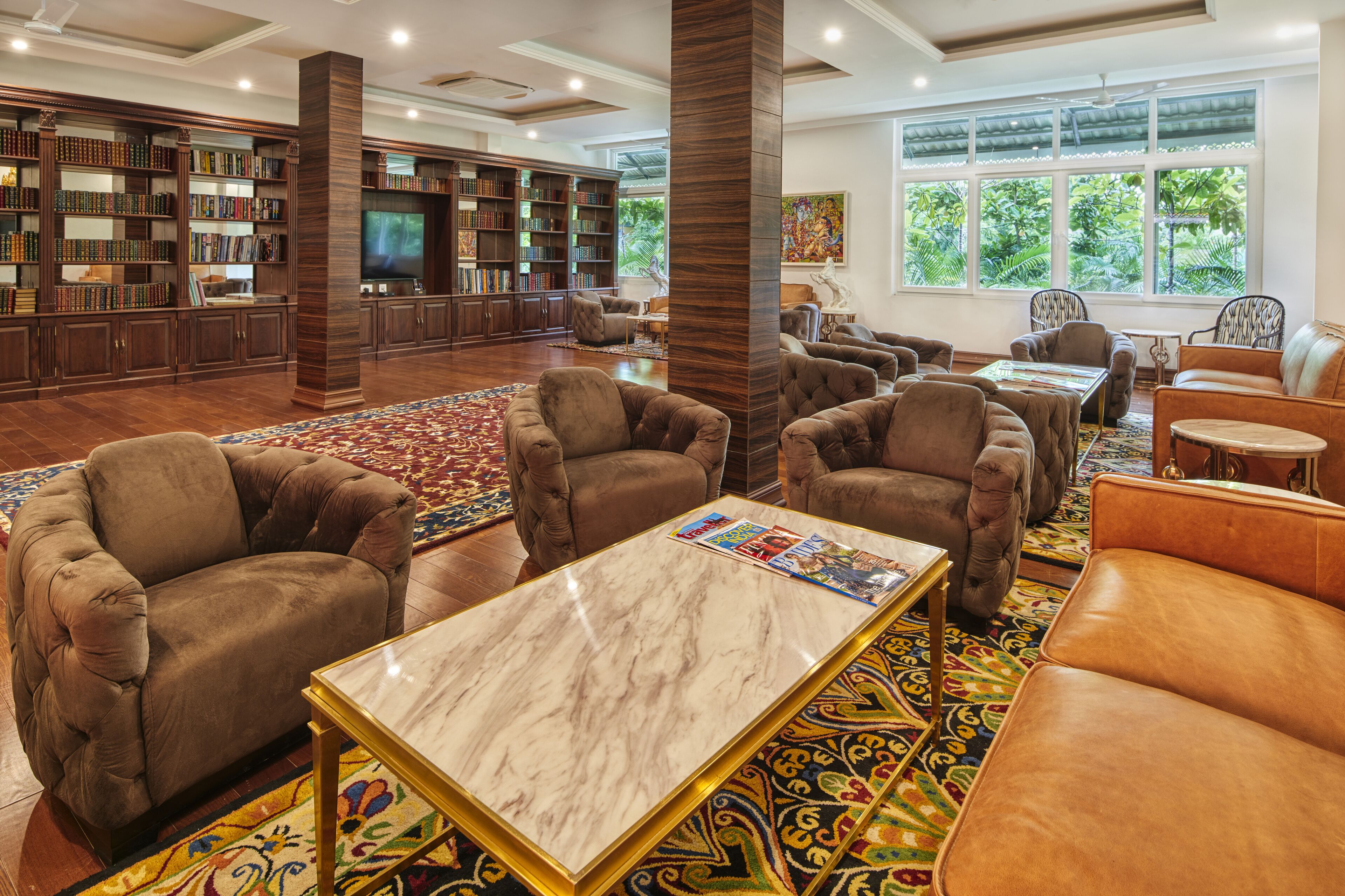 A library with bookshelves, comfortable seating, and a large window with a view of greenery.