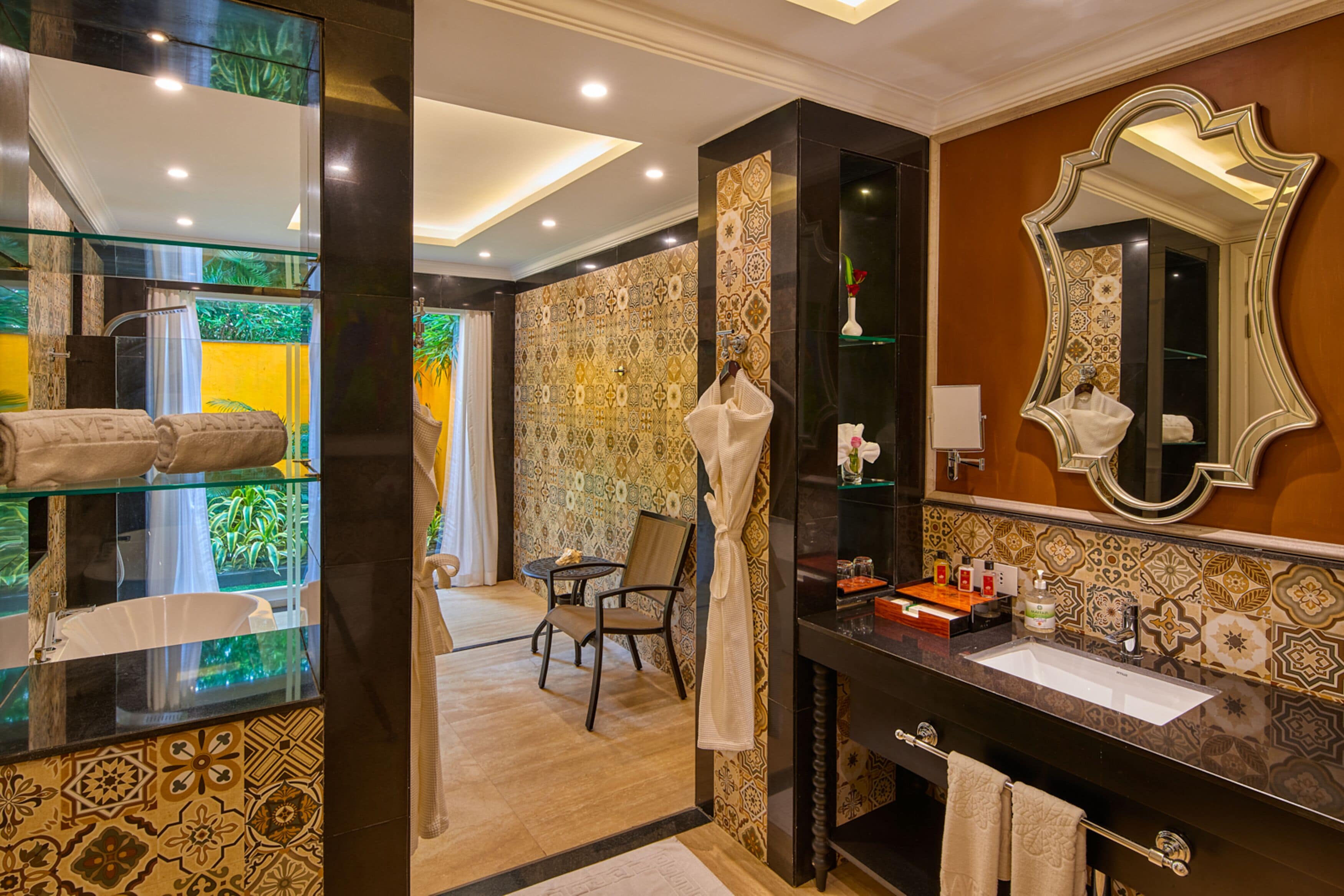 A bathroom with a glass enclosure, a sink, a mirror, and a chair.