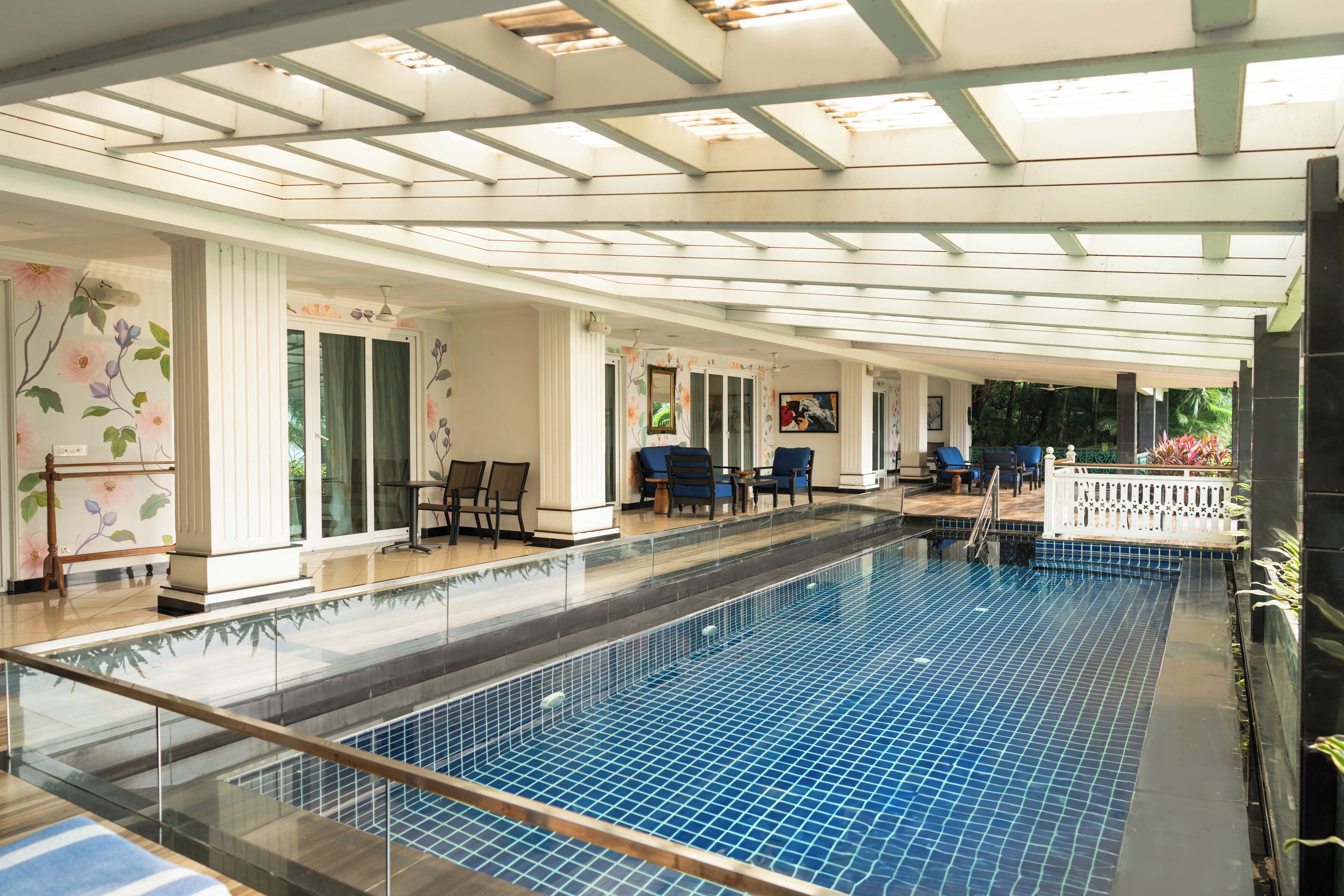 An indoor swimming pool with a glass barrier, seating areas, and a ceiling with skylights.