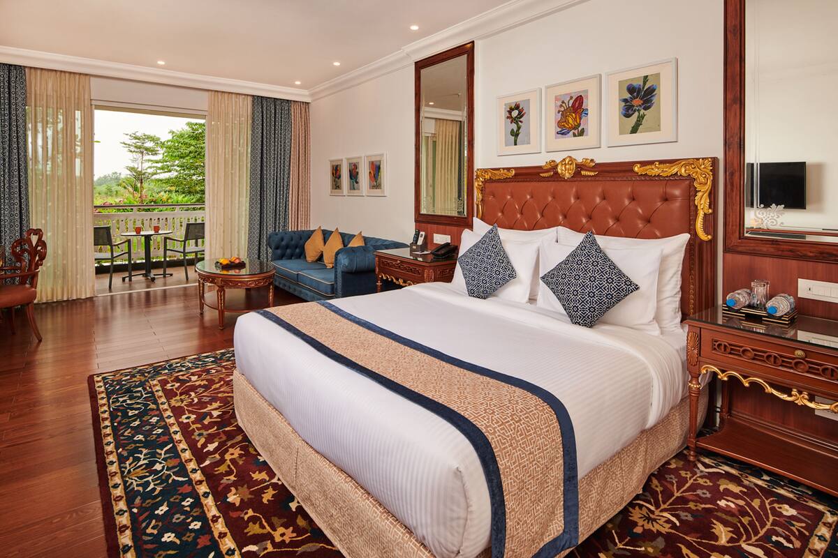 A spacious hotel room with a large bed, a balcony with a view, and a sitting area with a sofa and chairs.