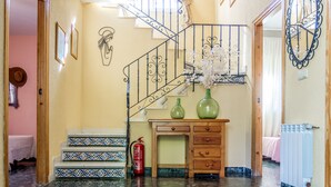 A spacious hallway with a polished floor, a staircase with a wrought iron railing, and a wooden cabinet with drawers. - Alojamiento La Veguilla (Úbeda)