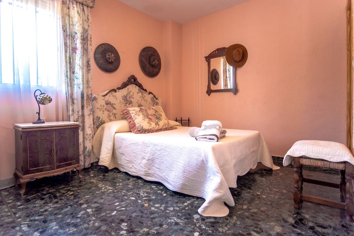 A bedroom with a bed, a nightstand, a chair, a dresser, and a mirror on the wall.