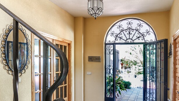 A hallway with a black metal staircase, a wooden bench, a decorative mirror, and a door leading to a garden. - Alojamiento La Veguilla (Úbeda)