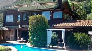 Una casa a due piani con piscina, veranda coperta e montagne sullo sfondo.