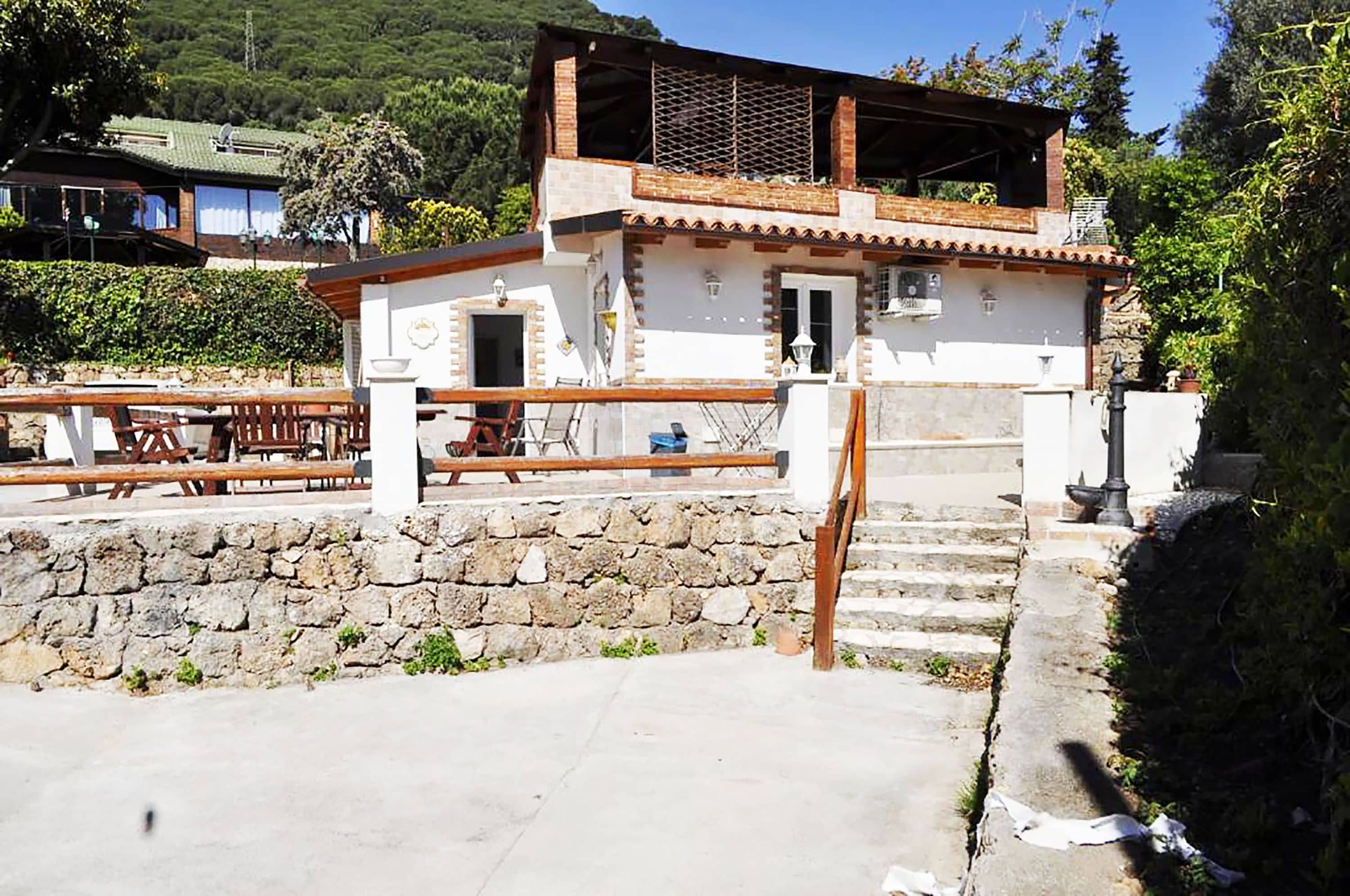 A two-story building with a stone wall, wooden staircase, and a balcony.