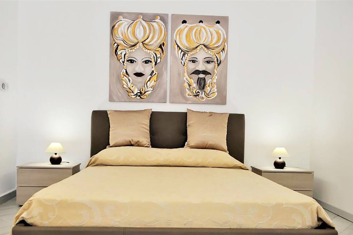 A bedroom with a large bed, two nightstands, two wall-mounted lamps, and two abstract paintings above the bed.