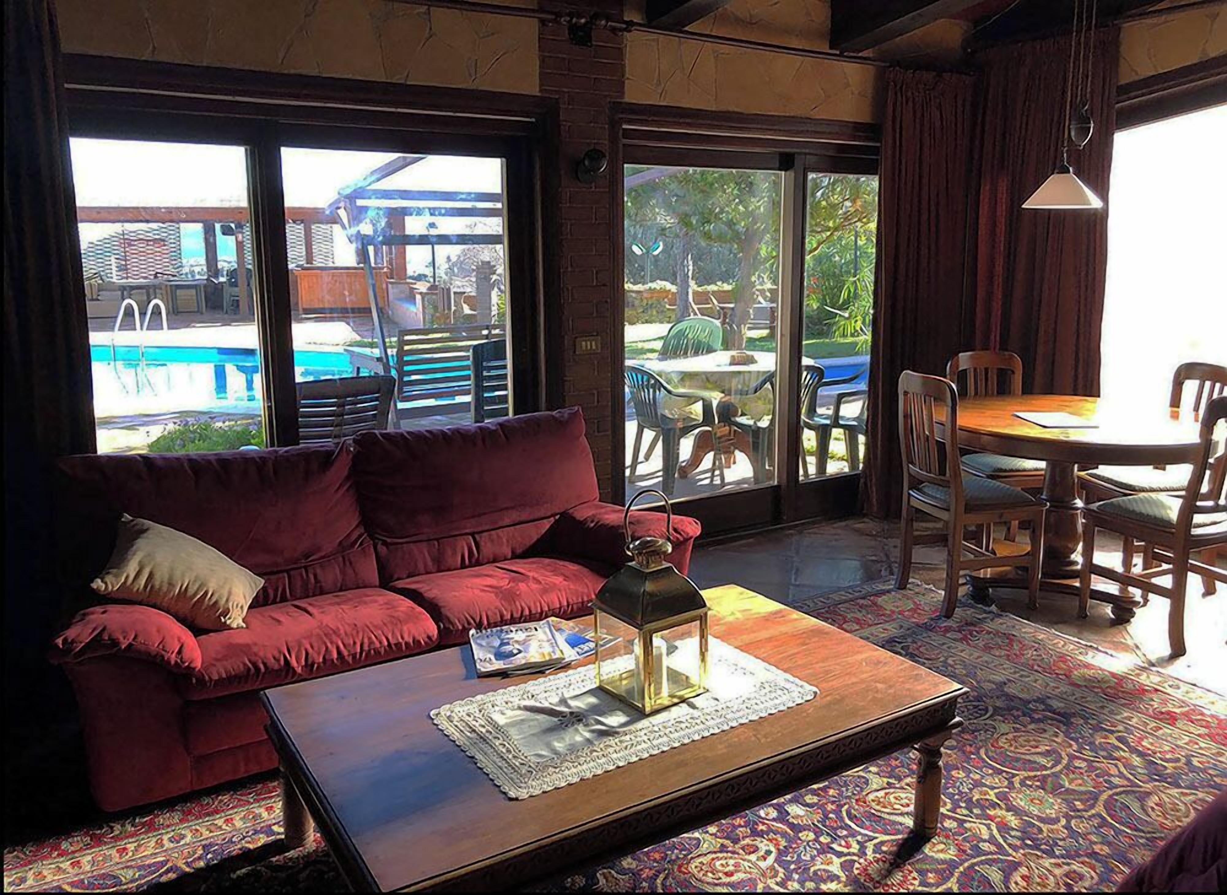 A cozy room with a red sofa, a wooden coffee table with a vase and magazines, and a view of an outdoor pool area.