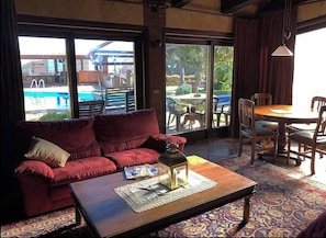 Una habitación acogedora con un sofá rojo, una mesa de centro de madera con un florero y revistas, y vistas a una zona de piscina al aire libre.