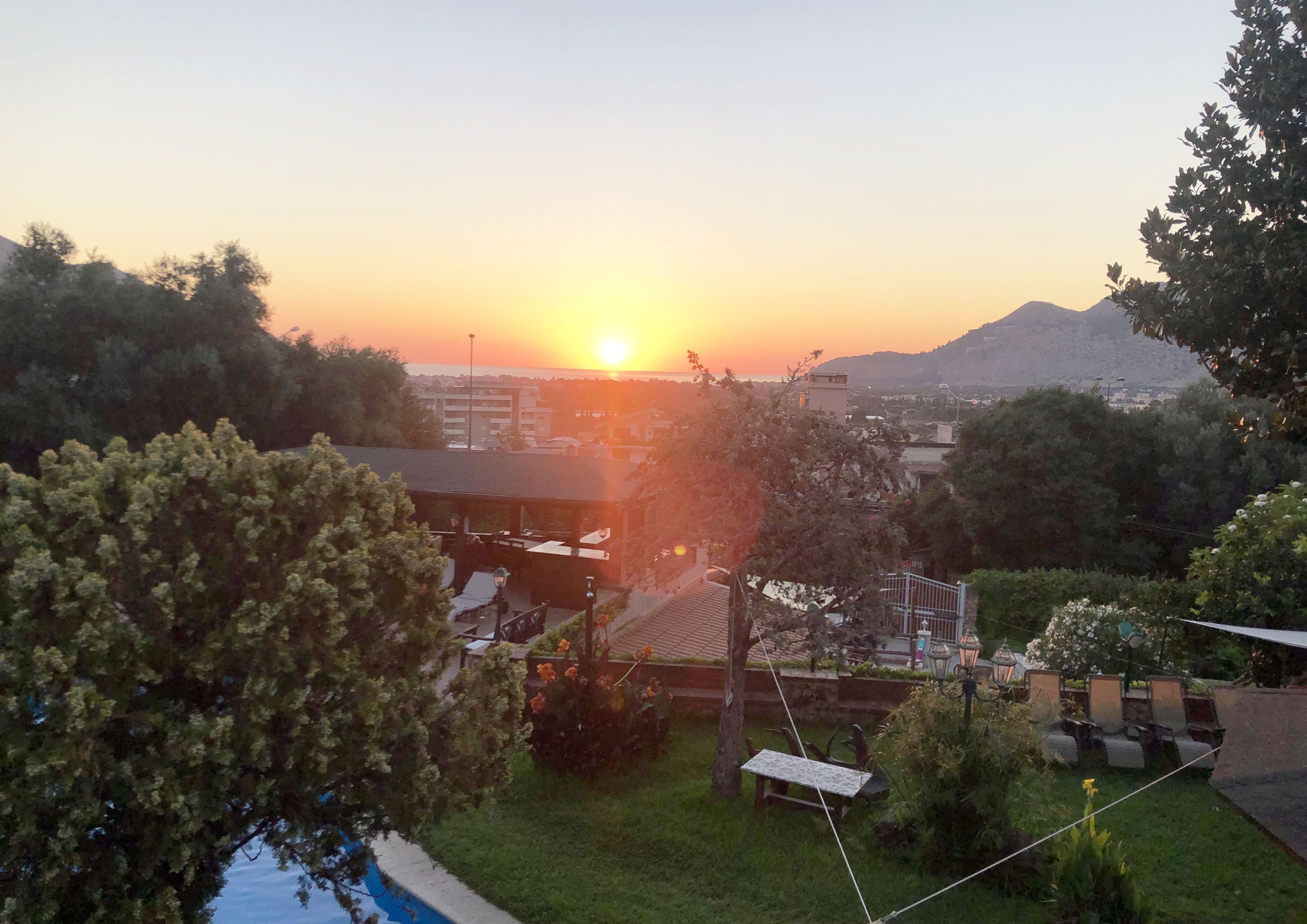 A sunset view from a residential area with a swimming pool, a gazebo, and a mountain in the background.