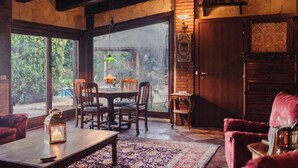 Una habitación acogedora con una mesa de madera, sillas, un sillón rojo y un amplio ventanal con vistas a zonas verdes.