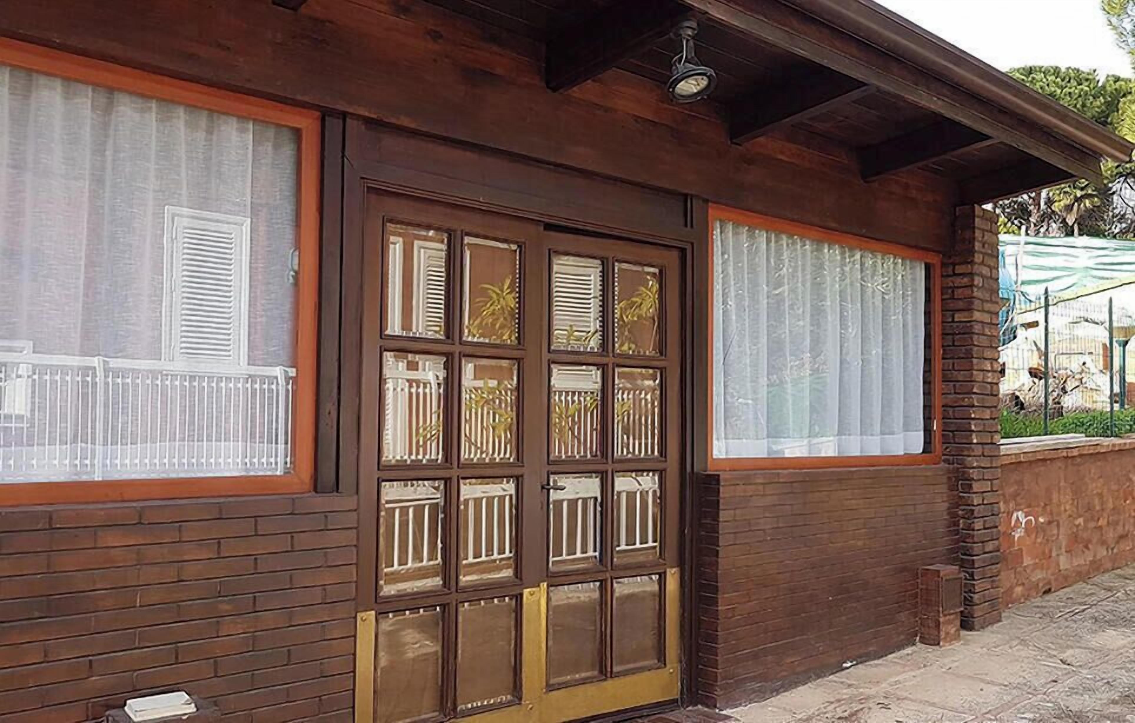 Ein hölzernes Gebäude mit einer großen Glastür, Fenster mit Rollläden und einer Backsteinmauer.
