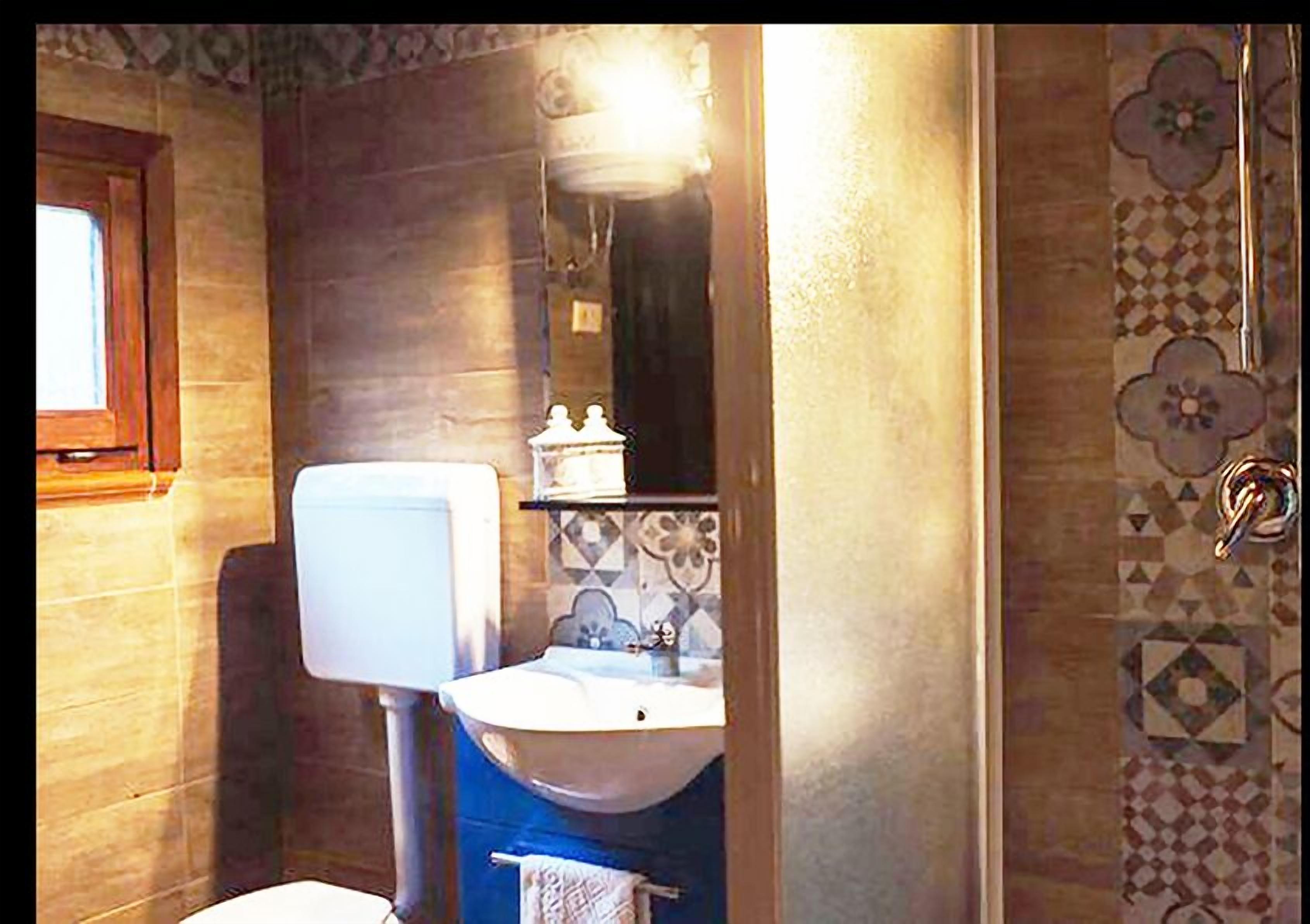 A bathroom with a toilet, sink, and mirror. There is a window above the toilet and a shower curtain with a floral pattern.