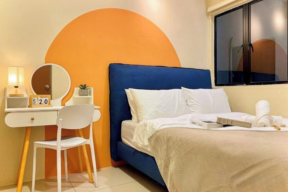 Una habitación de hotel con un cabecero azul, un escritorio blanco con un espejo, una silla y un reloj pequeño.