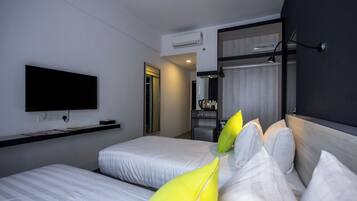 Habitación de hotel con dos camas, un televisor de pantalla plana montado en la pared y una pequeña zona de kitchenette.