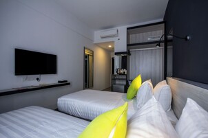 Habitación de hotel con dos camas, un televisor de pantalla plana montado en la pared y una pequeña zona de kitchenette.
