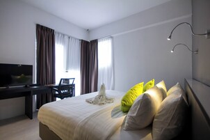 A hotel room with a bed, a desk with a computer, a TV, and curtains.