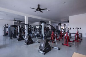 Un gimnasio con diferentes máquinas de cardio, pesas y un ventilador de techo.