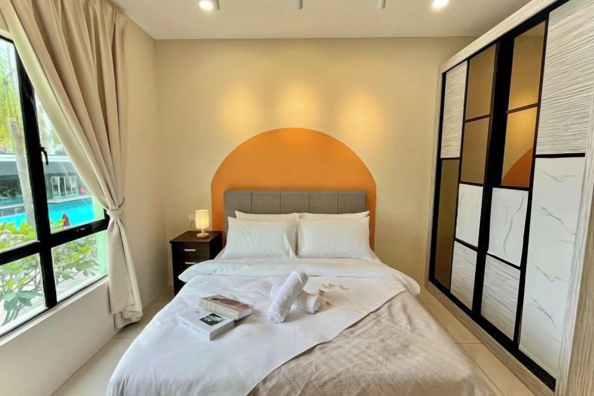 Una cama bien tendida con ropa de cama blanca, una mesita de noche con una lámpara, y vista a una piscina a través de un ventanal grande.