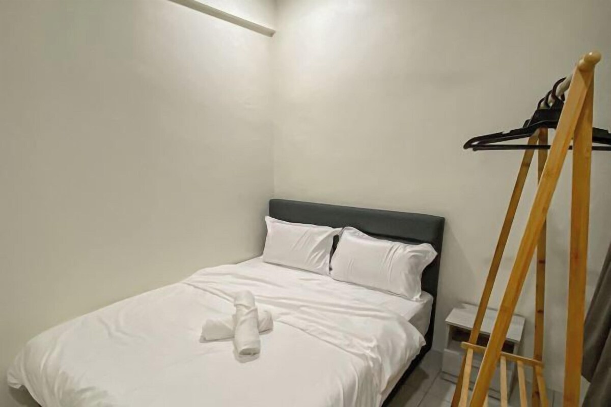 A neatly made bed with white linens and a towel, a wooden easel, and a small bedside table with a lamp.