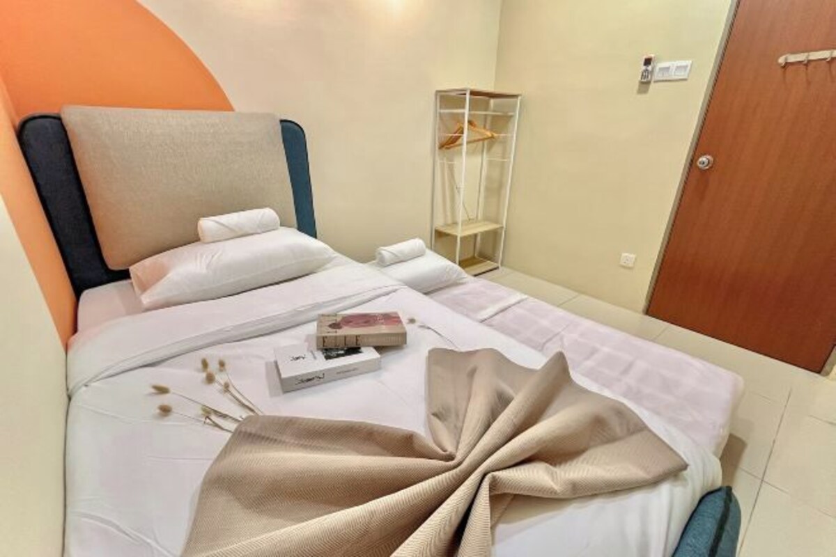 Una cama bien hecha con un edredón color beige, una almohada blanca y una mesita de noche con un libro y una caja de pañuelos.