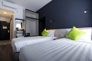Habitación de hotel con dos camas, un armario, un espejo y un pequeño escritorio con lámpara.