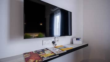 Un televisor montado en la pared sobre una estantería con revistas y un calendario.