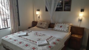 A neatly made bed with floral bedding, two bedside tables with lamps, and a window with curtains. - Lighthouse Guest (Galle)