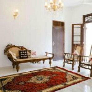 A room with a patterned rug, a wooden sofa, a wooden chair, and a chandelier. - Lighthouse Guest (Galle)