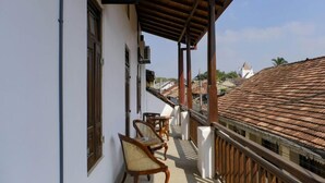 A balcony with two wicker chairs and a small table, overlooking a traditional tiled roof building. - Lighthouse Guest (Galle)