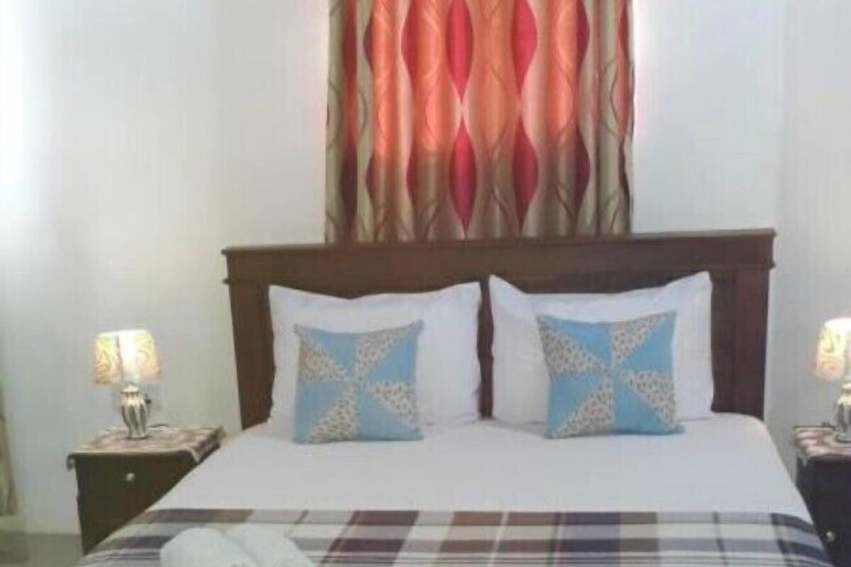 A neatly made bed with a plaid bedspread, two pillows with a geometric pattern, and a pair of rolled towels on the bed.