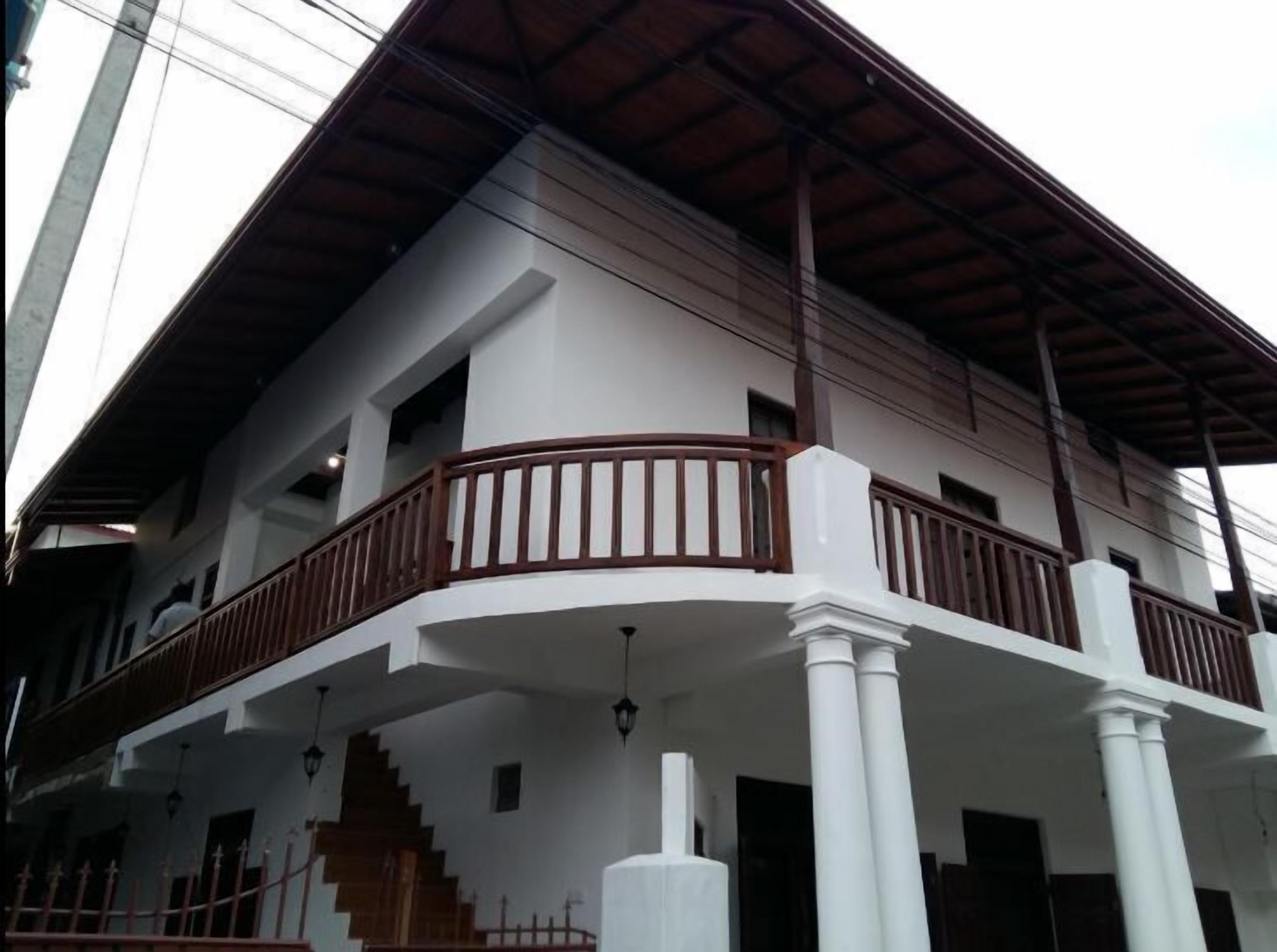 Un edificio de varios pisos con fachada blanca, barandillas de balcón de madera y un piso superior cubierto.