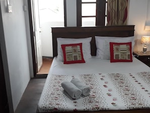 A neatly made bed with floral bedding, two pillows with red borders, and a pair of folded towels on the bed. - Lighthouse Guest (Galle)
