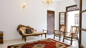 A room with a wooden sofa, two wooden chairs, a patterned rug, a chandelier, and a traditional door. - Lighthouse Guest (Galle)