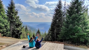Two people sitting on a wooden deck with a scenic view of mountains and trees. - Wellness Hotel Garni Krone (Baiersbronn)