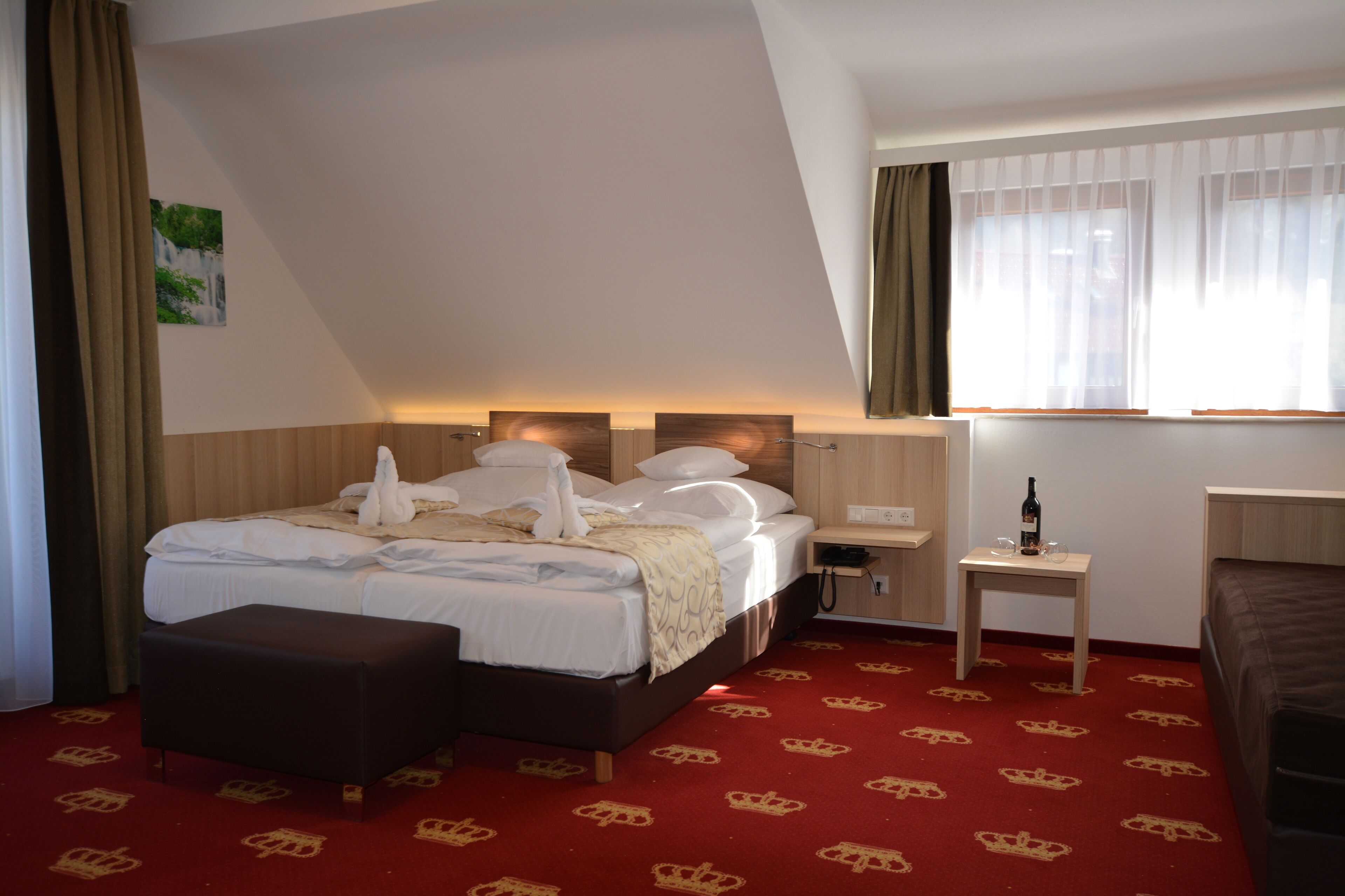 A hotel room with a bed, bedside table, and a small table with a bottle and glasses.