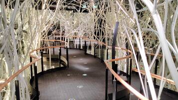 A corridor with a curved railing, white branches hanging from the ceiling, and a tiled floor.