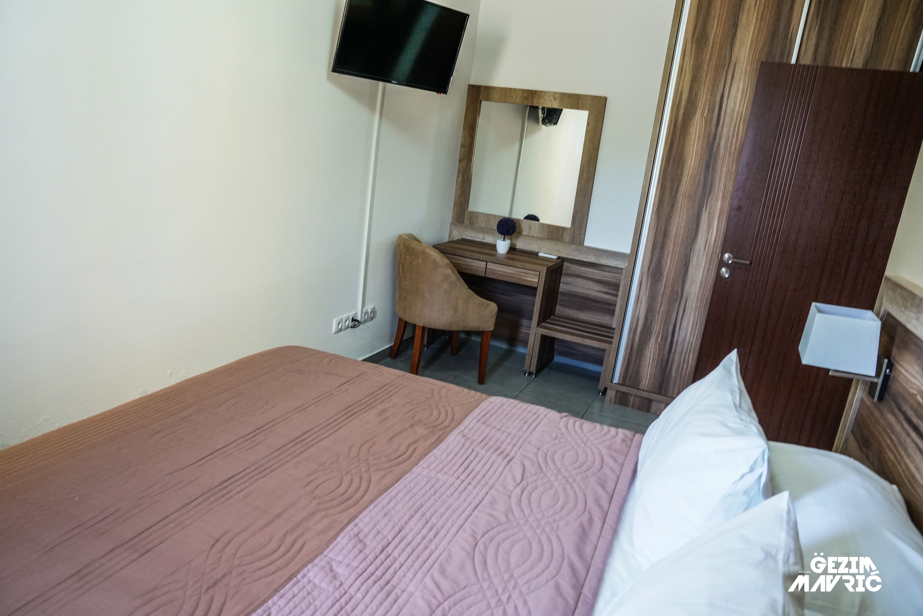 A bedroom with a bed, a desk, a chair, a mirror, and a wardrobe.