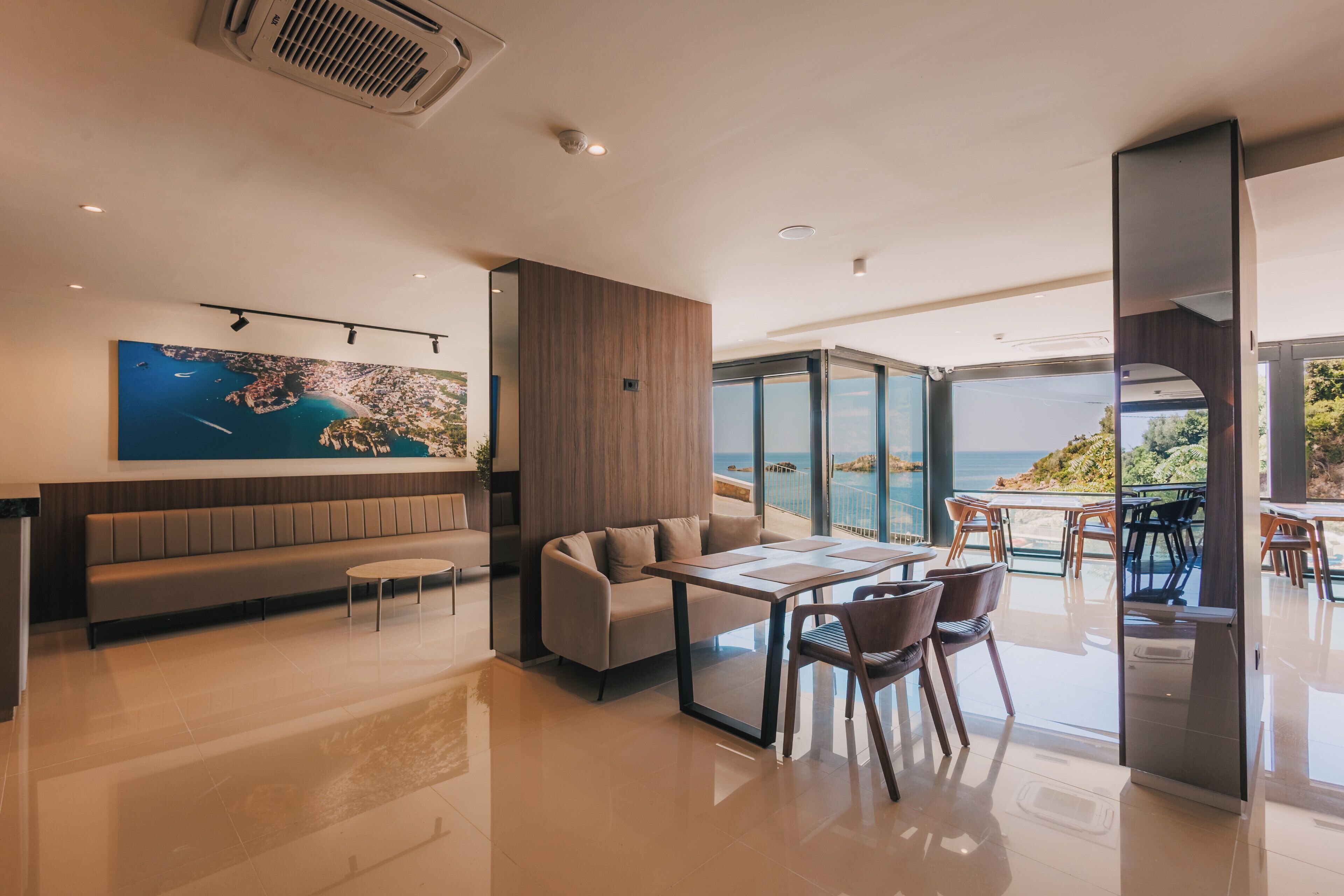 A modern interior with a seating area, a dining table, and a large window offering a view of the sea.
