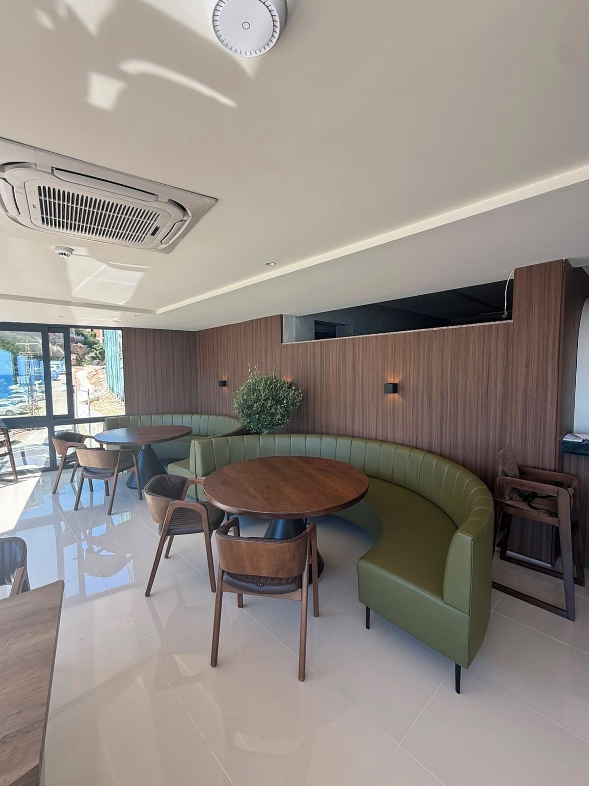 Een modern interieur met een gebogen zitgedeelte in groen, een ronde houten tafel en een aan het plafond bevestigde airconditioning.